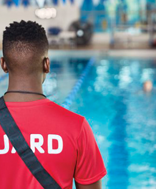 African American Lifeguard with red shirt facing pool