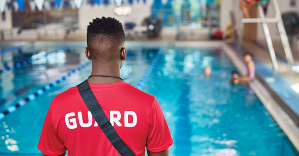 African American Lifeguard with red shirt facing pool