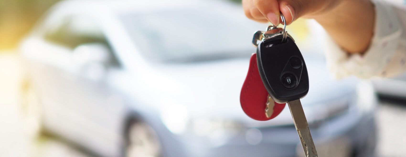 Set of car keys in foreground with a car in the background